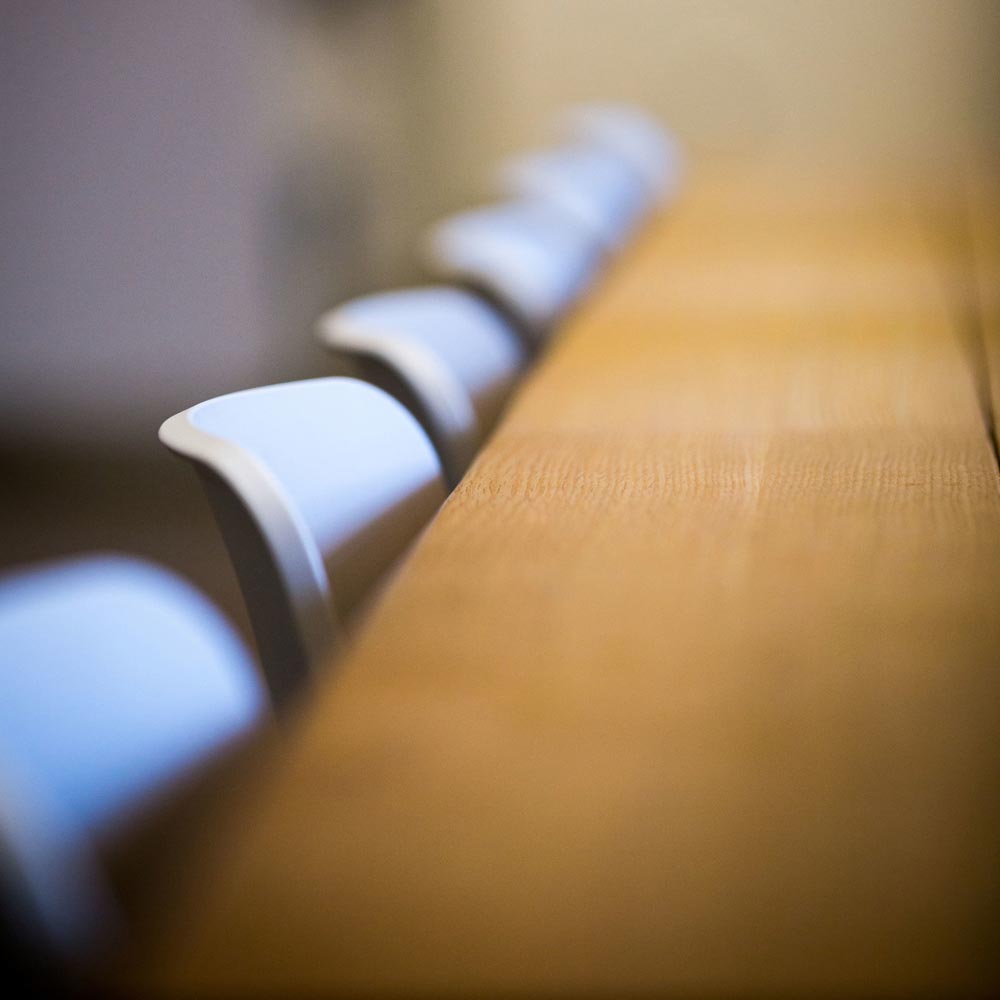 A blurry, abstract photo of the backs of chairs lined up against a conference table.