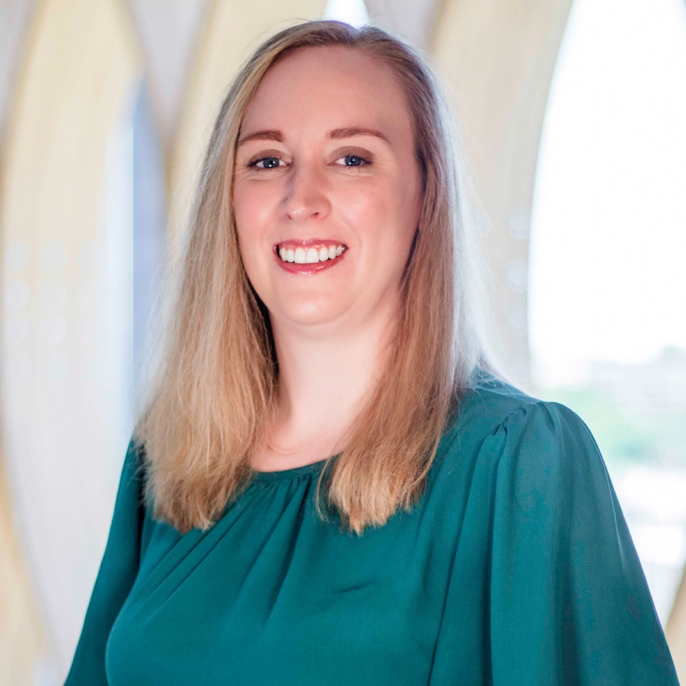 A smiling Erin Ray, DO of Family Medicine with light brown hair, wearing a green blouse, against a softly blurred background.