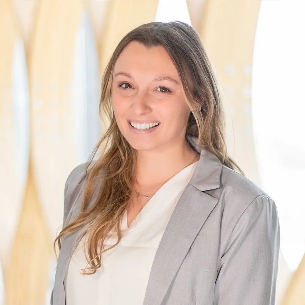 Samantha Middleton, PA-C, with long light brown hair, smiles while wearing a light gray blazer over a white blouse, standing in front of a blurred light-colored background.