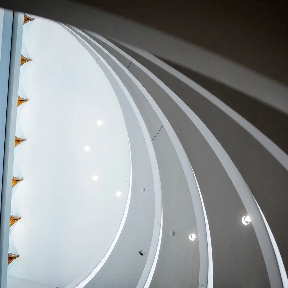Curved white architectural lines and arches create a modern, abstract ceiling reminiscent of innovative spaces where you might think healthcare, featuring small recessed lights and gold triangular accents on the left.
