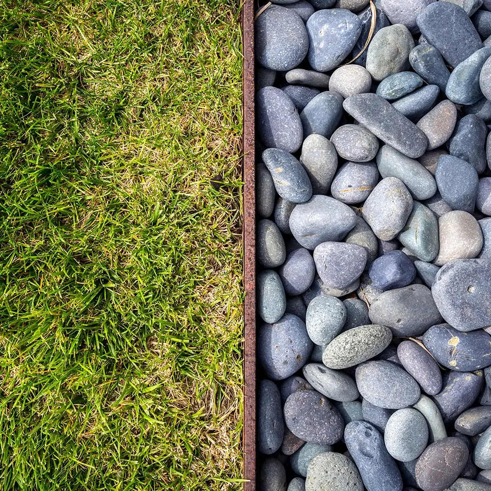 A close-up view showing a neat border separating vibrant green grass on the left from smooth gray river rocks on the right.