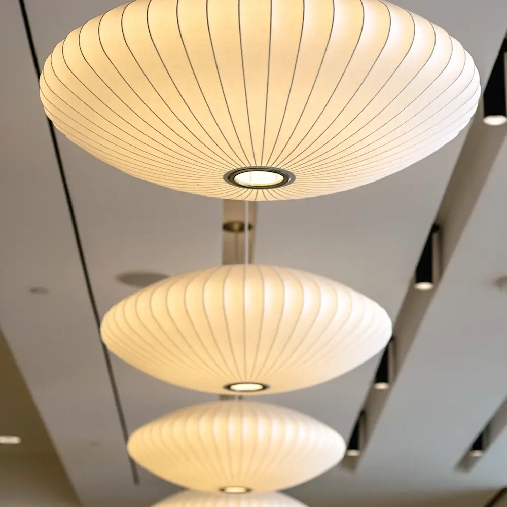 Three large, round, white pendant lights with ribbed textures hang in a row from the ceiling of a modern interior space, creating a soft, warm glow.