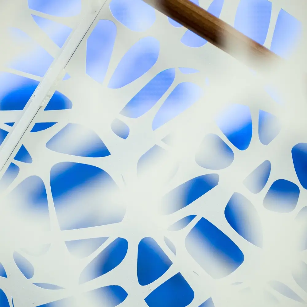 Abstract synaptic pattern close-up of a white, organic-patterned panel with irregular cutouts, set against a blue background. A wooden handrail runs diagonally across the upper part, evoking a calm, think healthcare-inspired environment.