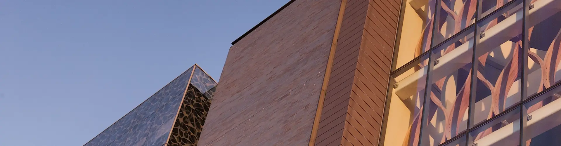 Close-up view of modern building facades featuring geometric shapes, glass panels, and textured surfaces, set against a clear blue sky.