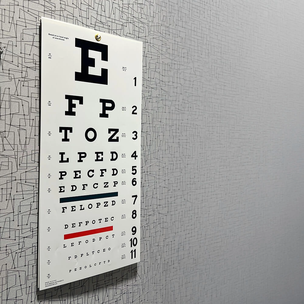 An eye chart with rows of letters decreasing in size is mounted on a patterned gray wall, used for vision tests in clinics or optometrist offices.