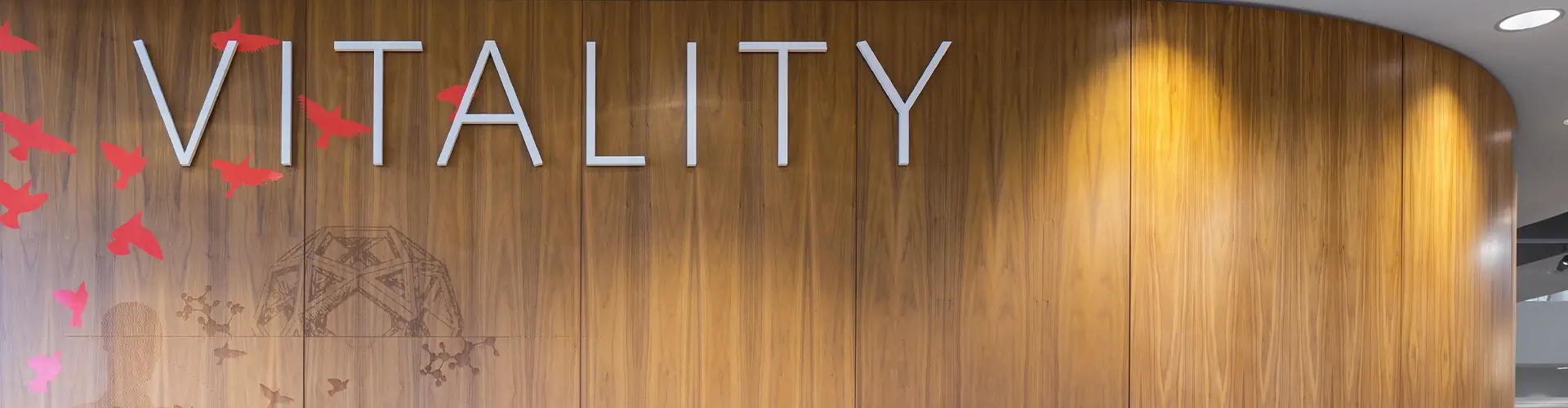 A wooden wall with the large word VITALITY in metallic letters, red bird silhouettes on the left, and warm spotlighting from above.