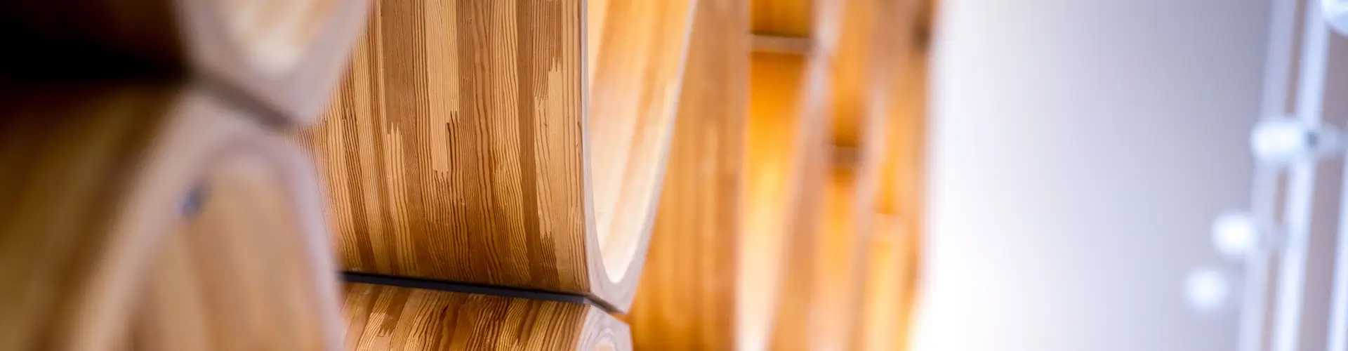 Close-up of smooth, light-colored wooden panels with visible grain patterns, arranged in a geometric design against a white background with blurred circular light spots on the right.