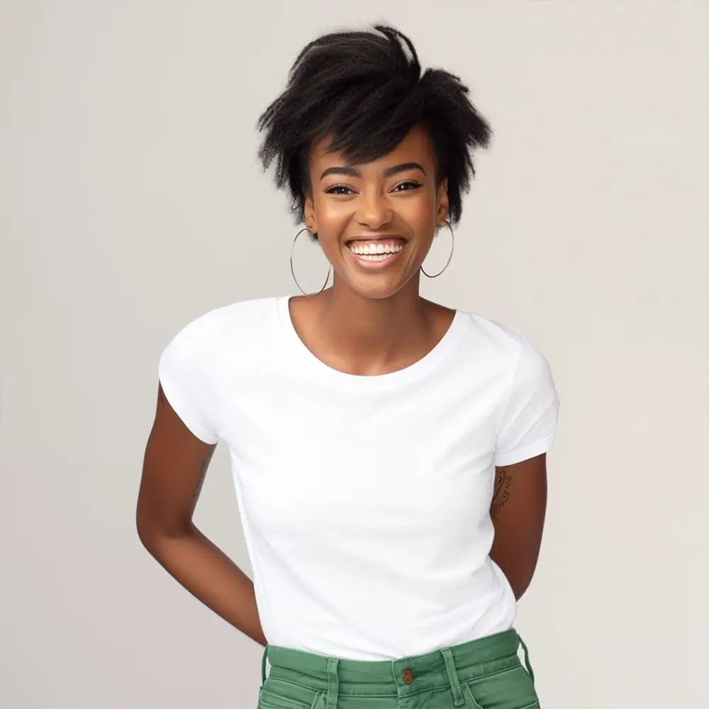 A smiling woman with short natural hair, wearing hoop earrings, a white t-shirt, and green pants, stands against a plain light background with her hands behind her back.