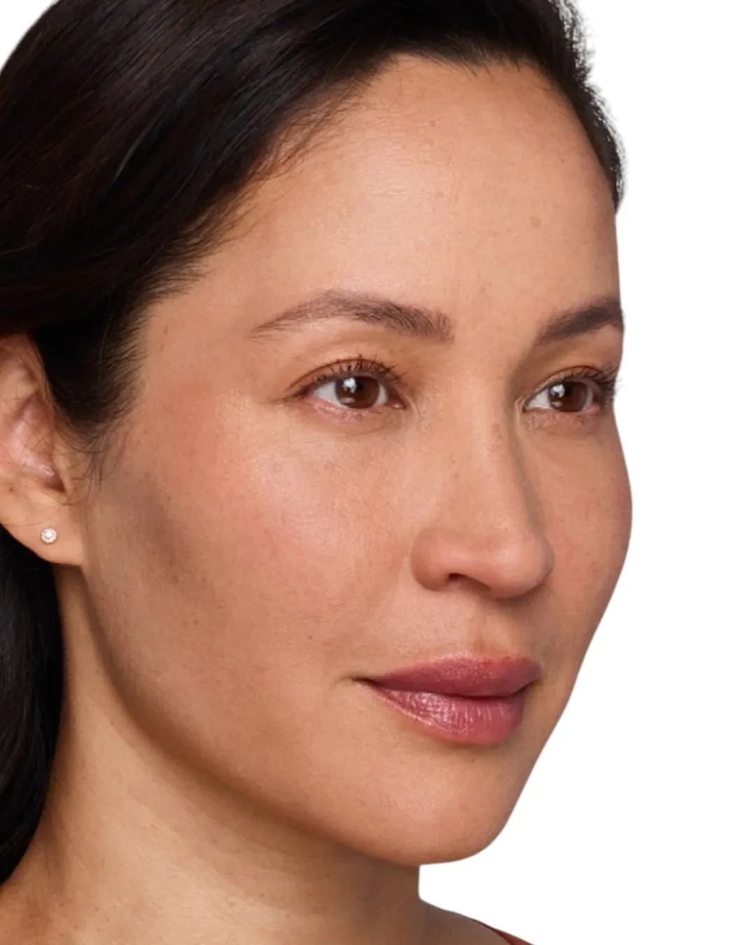 A woman with medium skin tone and dark hair looks slightly to the side. She has natural makeup, glossy lips, and a small stud earring. The background is plain white.