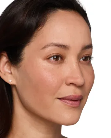 A woman with medium skin tone, dark hair, and subtle makeup looks slightly to the side. She wears a small stud earring, and her expression is calm with a gentle smile. The background is white.