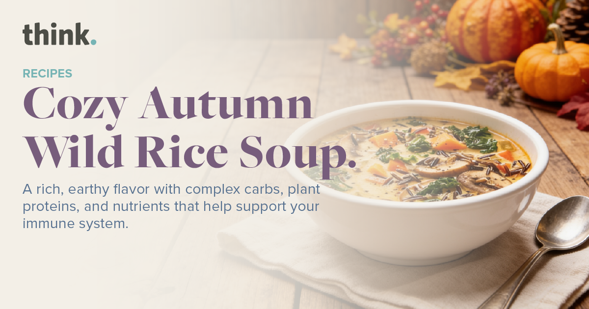 A bowl of wild rice soup with vegetables sits on a table, surrounded by autumn decorations including pumpkins and leaves. Text promotes a cozy autumn soup recipe that supports the immune system.