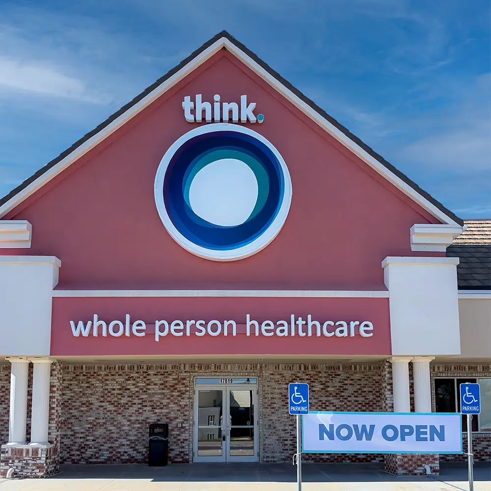 Exterior of a think. whole person healthcare clinic with a NOW OPEN banner by the entrance.